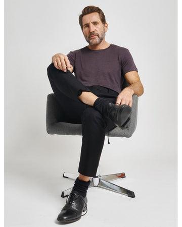 Homme barbu assis dans un fauteuil et jambes croisées qui porte un t-shirt couleur gris charbon coupe droite en lin de la marque française durable Splice.