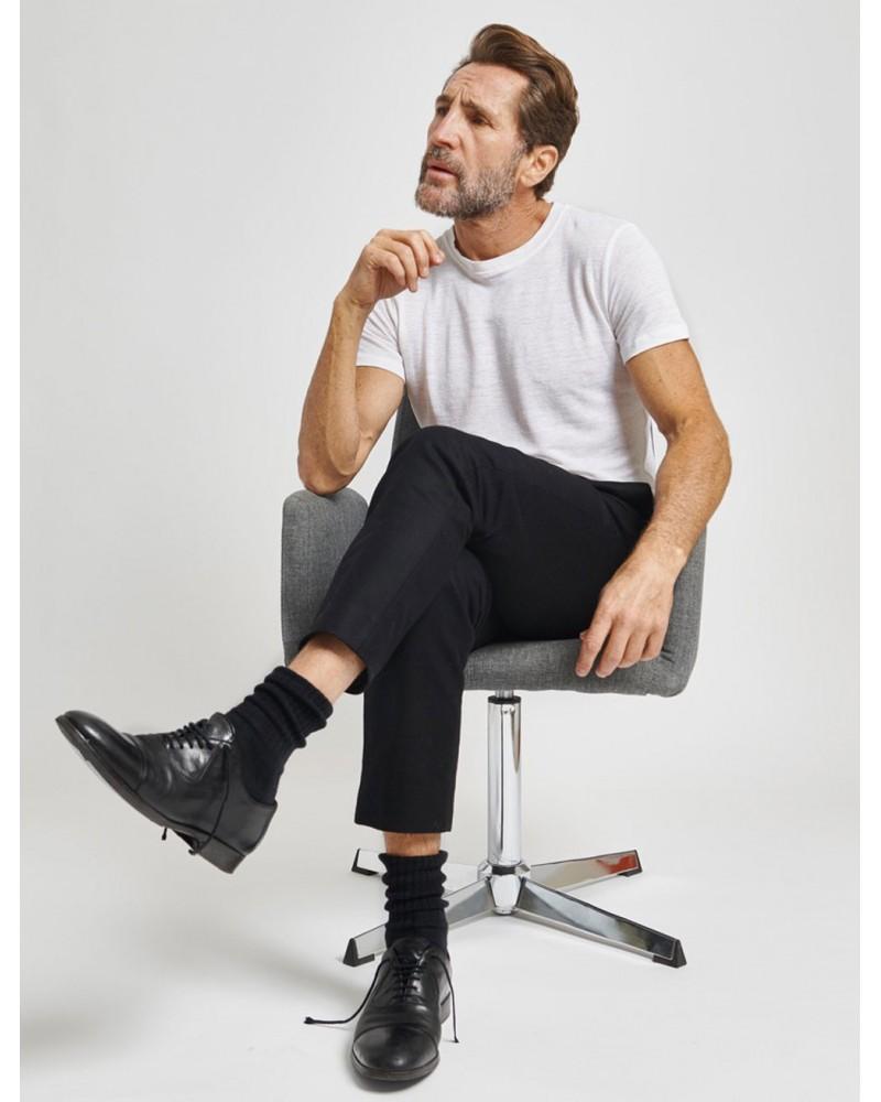 Homme brun avec une barbe assis et jambes croisées portant un t-shirt blanc non cintré et léger en lin cultivé, tissé et teint en France. Il est proposé par la marque Française écoresponsable Splice.