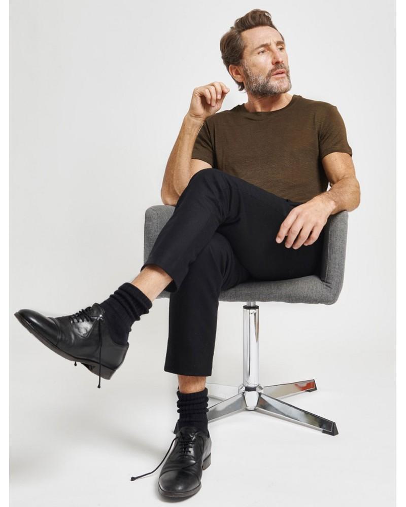Homme barbu assis sur un fauteuil avec les jambes croisées portant un t-shirt marron en lin français.