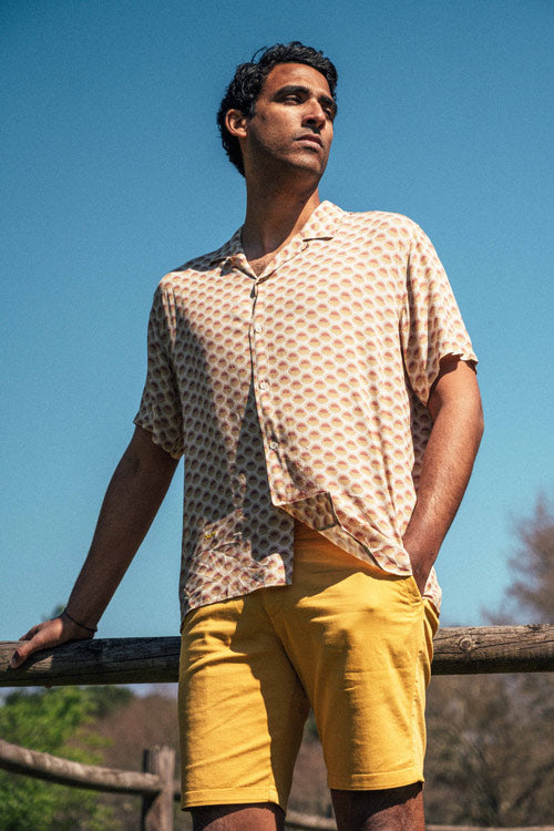 Photo de plein pied d'un mannequin portant une chemisette pour homme imprimé soleil sur fond beige faite en viscose EcoVero et fabriquée au Portugal.