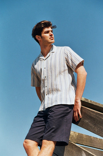 Photo d'un mannequin portant une chemisette homme rayée bleu et beige en coton bio et fabriquée au Portugal.