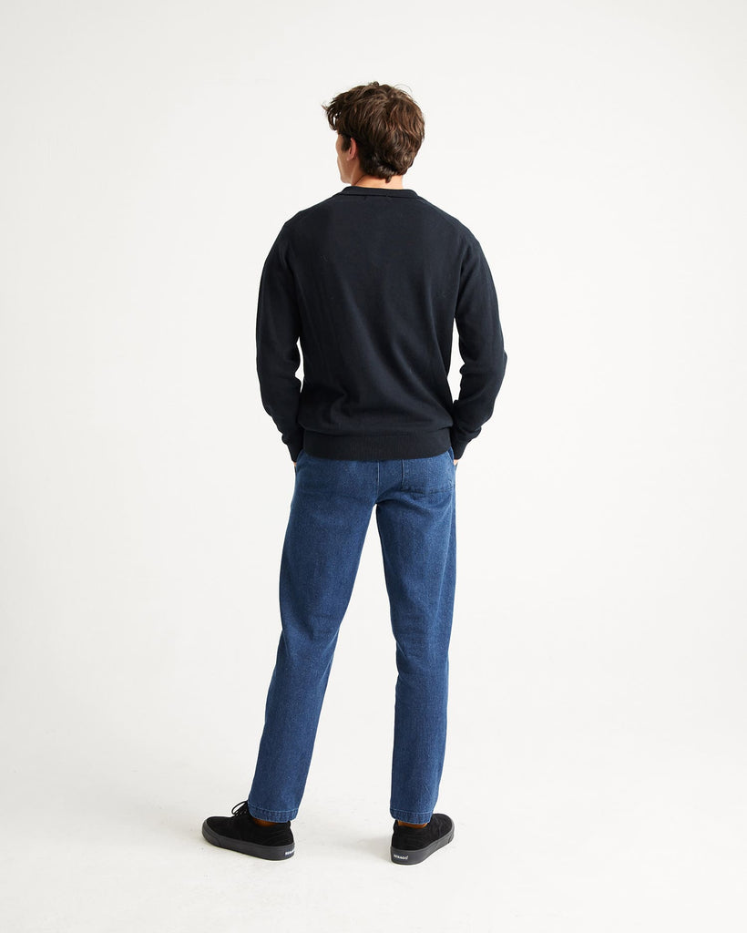 Un homme de dos porte un jean et un pull avec col polo bleu marine de la marque Thinking Mu.