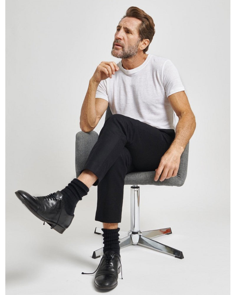 Homme barbu en pleine réflexion, assis et croisant les jambes. Il porte un t-shirt manches courtes blanc en lin non cintré réalisé par Splice, une marque responsable de lin.