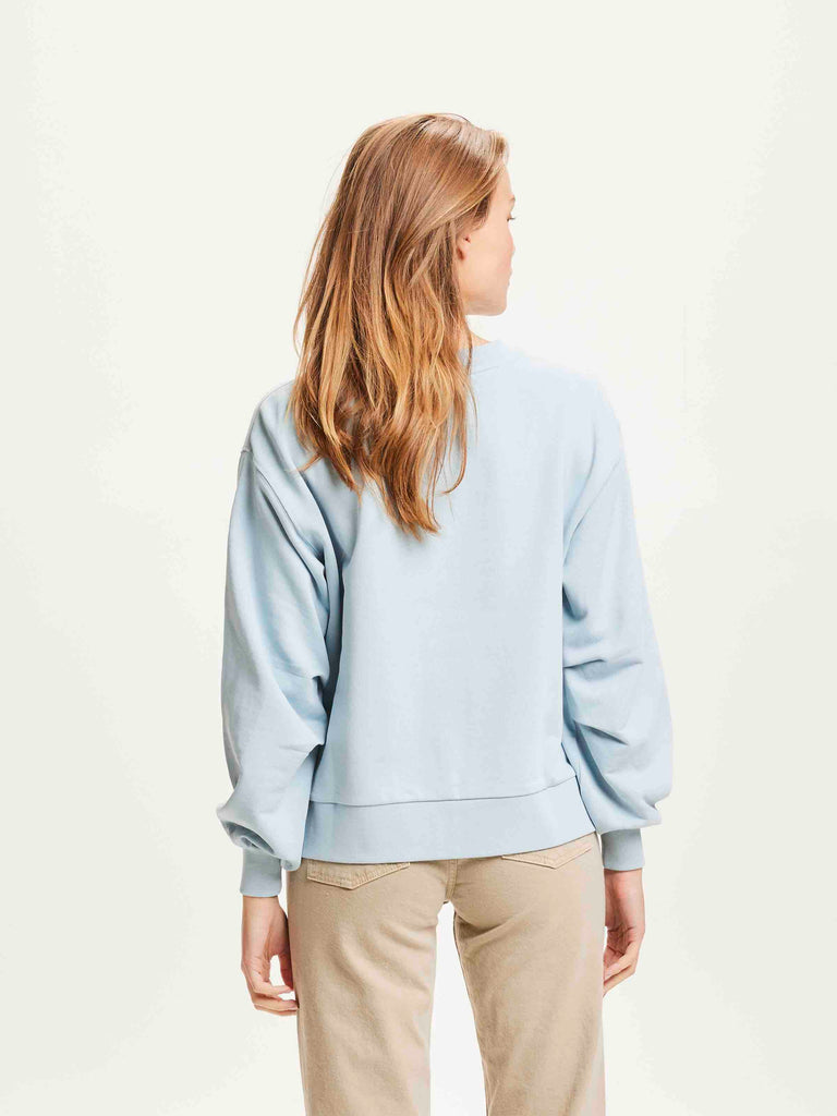 Une femme de dos porte un sweat shirt bleu ciel de la marque Knowledge Cotton Apparel.