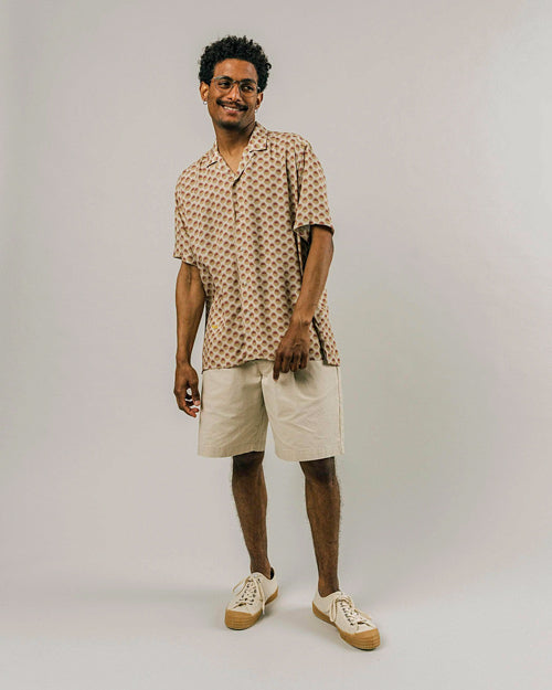 Photo de plein pied d'un mannequin portant une chemisette pour homme imprimé soleil sur fond beige faite en viscose EcoVero et fabriquée au Portugal.