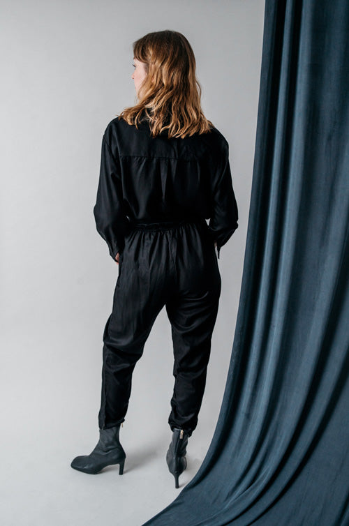 Photo d'un mannequin de dos portant une combi pantalon femme noire en lyocell fabriquée au Portugal de la marque Cossac.
