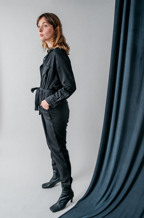 Photo d'un mannequin de profil portant une combi pantalon femme noire en lyocell fabriquée au Portugal de la marque Cossac.
