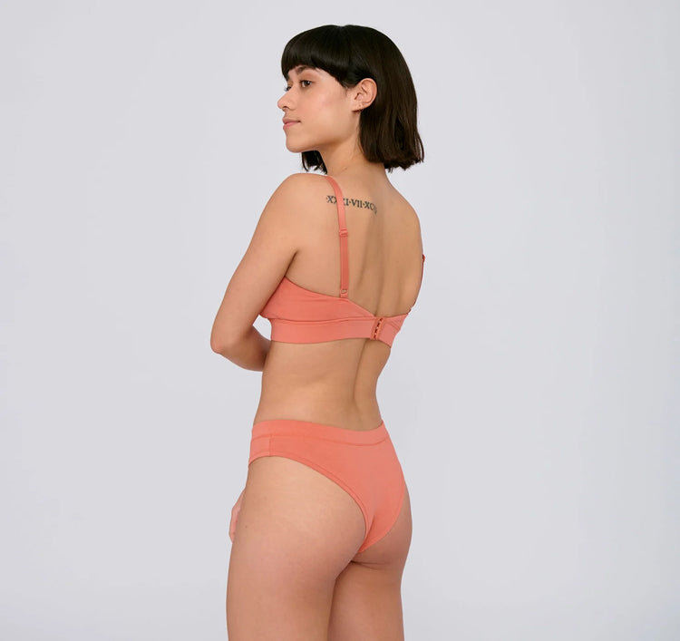 Photo d'un mannequin de profil portant une culotte en coton bio corail de la marque organic basics.