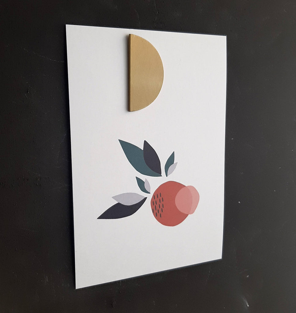 Carte postale imprimée en sérigraphie avec un dessin de pomme tenu par un bijou mural aimanté..