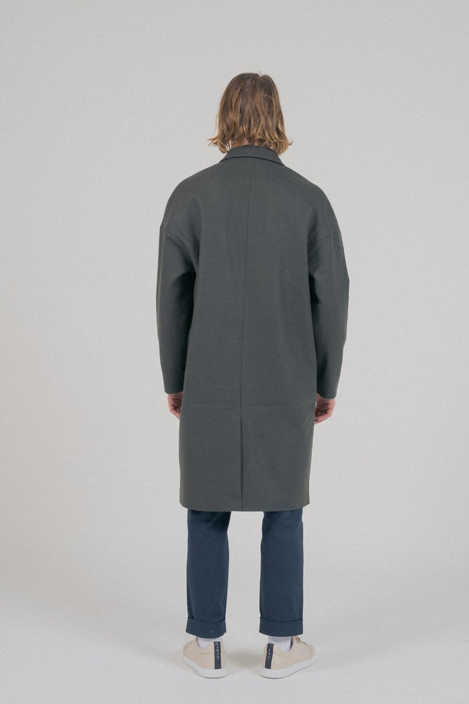 Un mannequin homme de dos porte un manteau long oversize kaki de la marque Noyoco.