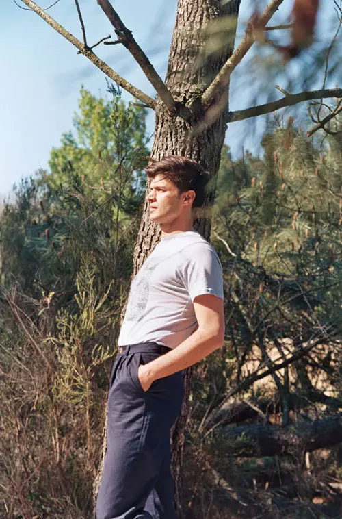 Un homme porte un pantalon bleu marine posé contre un arbre.