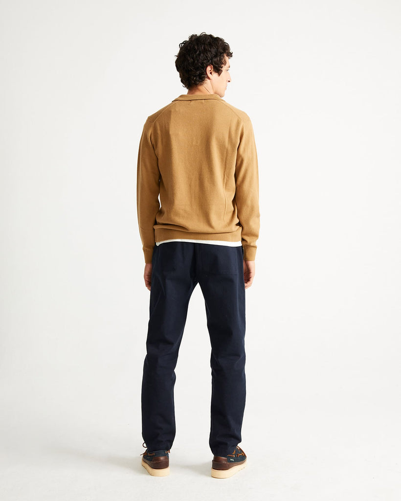 Un homme de dos porte un jean et un pull avec col polo ocre de la marque Thinking Mu.