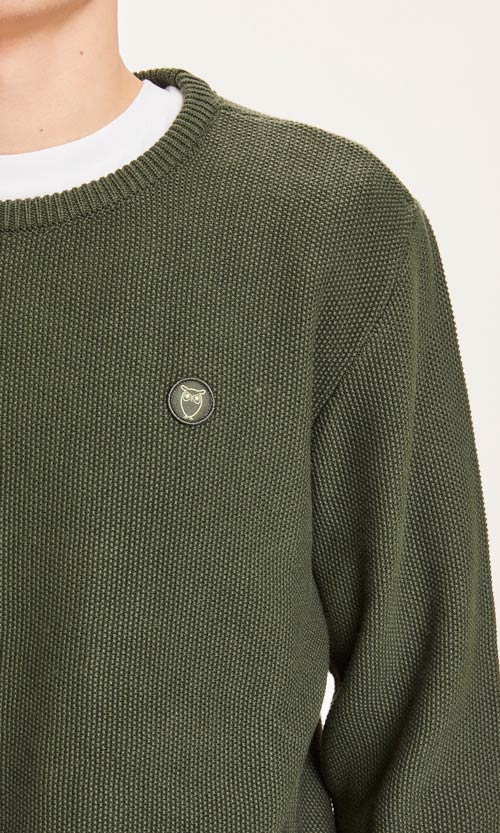 Photo zoomée d'un mannequin portant un pull en coton bio pour homme couleur vert sapin de la marque knowledge cotton apparel.