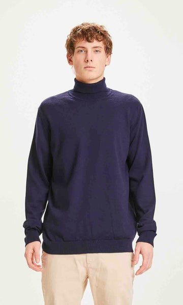 Un homme de face porte un pull col roulé marine de la marque Knowledge Cotton Apparel.