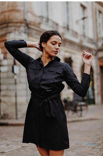 Une femme qui a la main dans les cheveux porte une robe noire de la marque Mariannette.