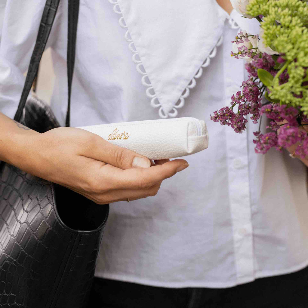 Une femme porte une trousse blanche en cuir végétal de la marque Alénore.