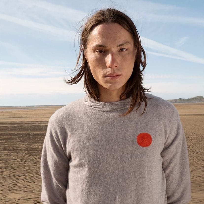 Mannequin portant un pull gris avec un rond rouge de la marque Loreak Mendian.