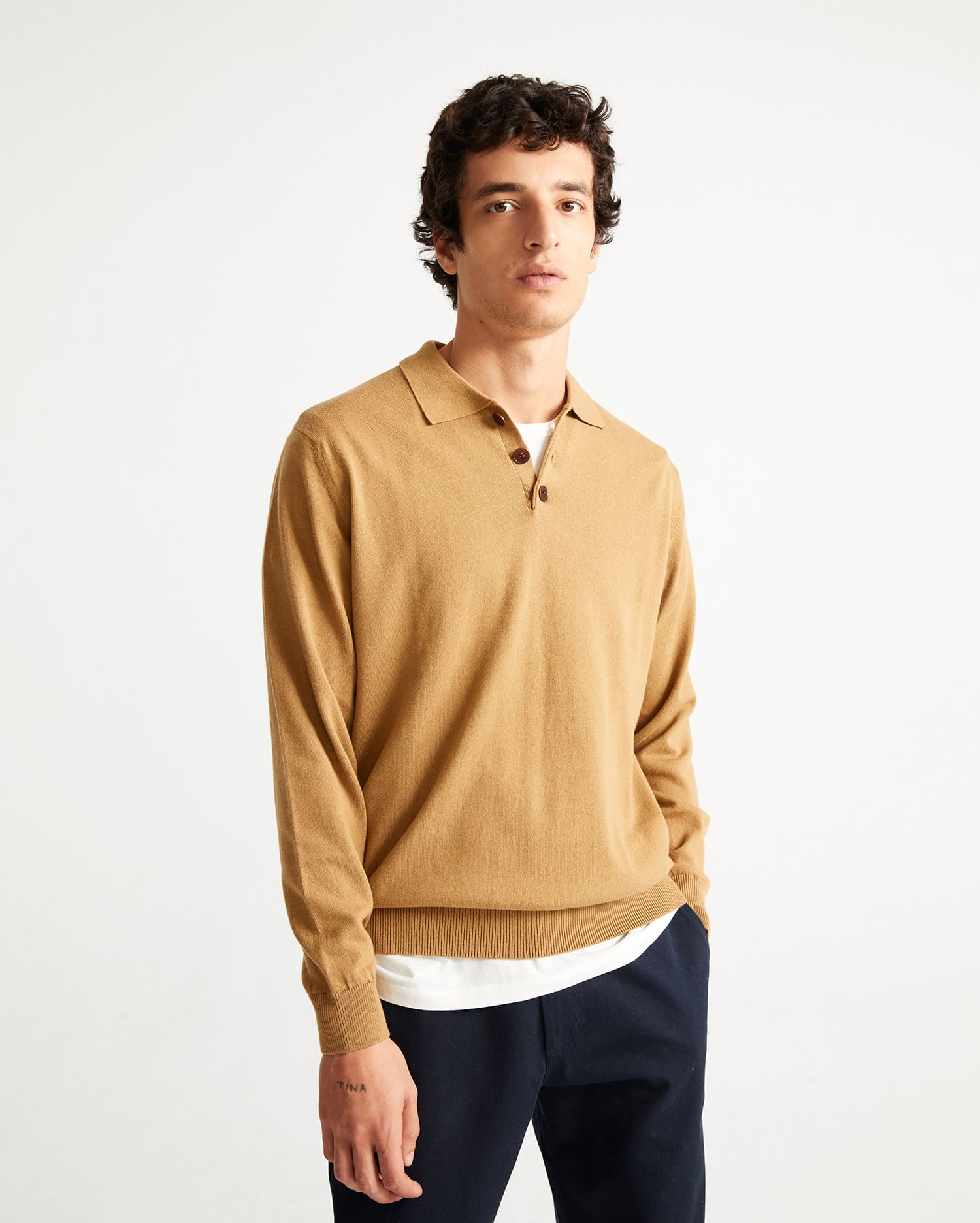 Un homme debout qui porte un pull avec un col polo de couleur ocre de la marque Thinking mu.
