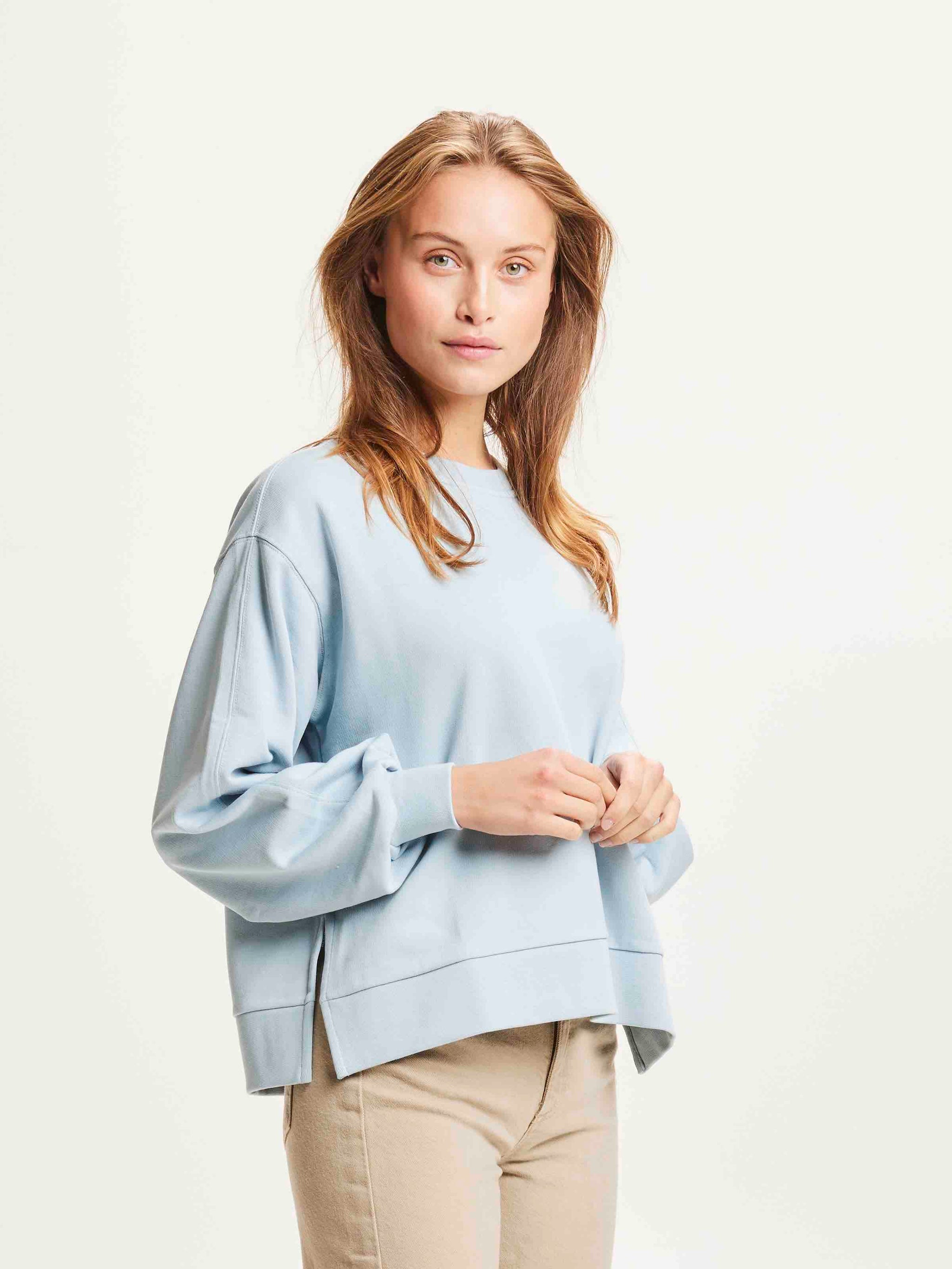 Une femme porte un sweat shirt bleu ciel de la marque Knowledge Cotton Apparel.