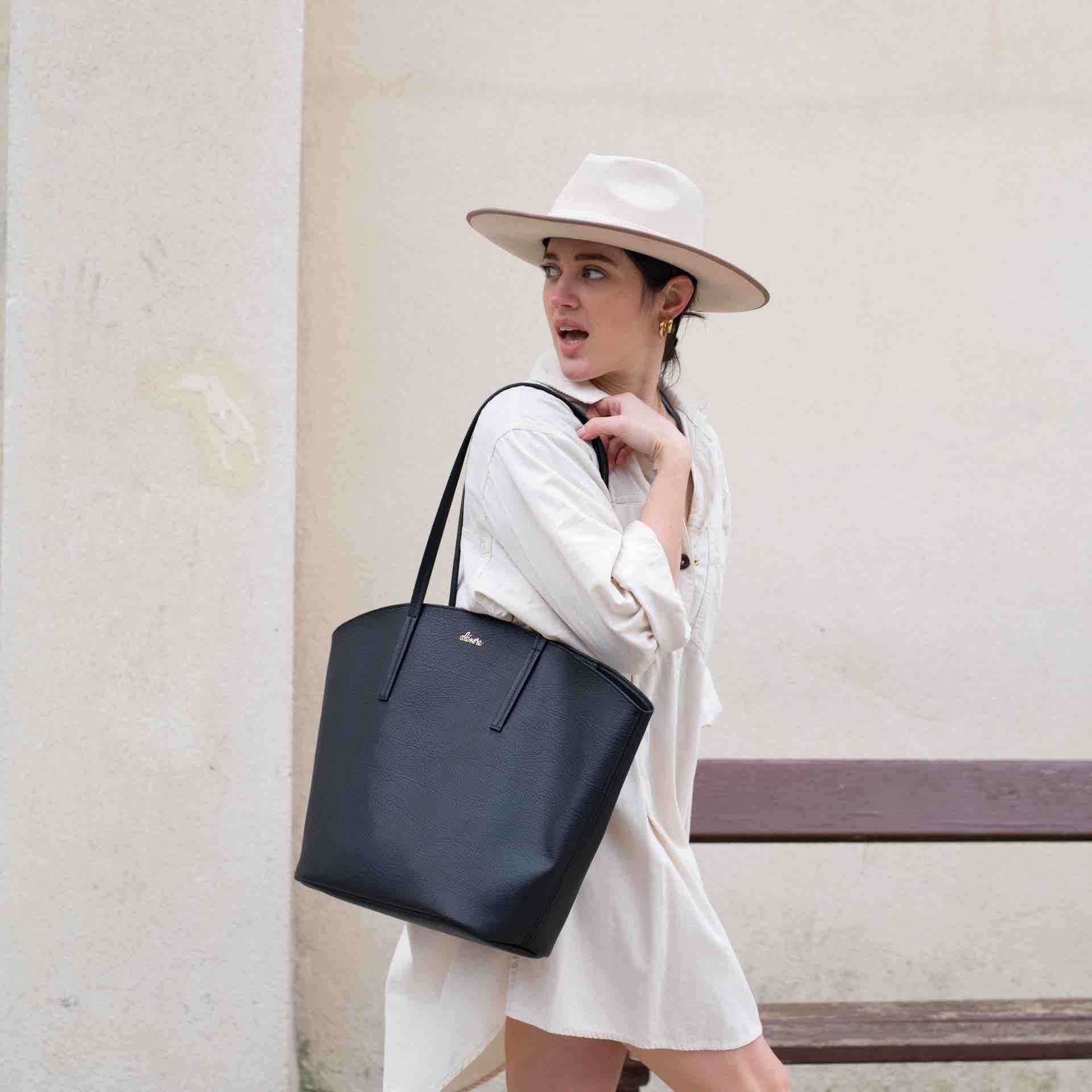 Une femme porte à l'épaule le cabas Mimosa en cuir végétal noir de la marque Alénore.